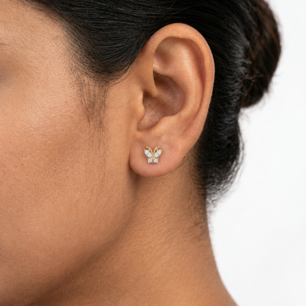 Close-up of a woman's ear wearing a 14k solid yellow gold butterfly stud earring with natural diamond wings, showing its dainty size.
