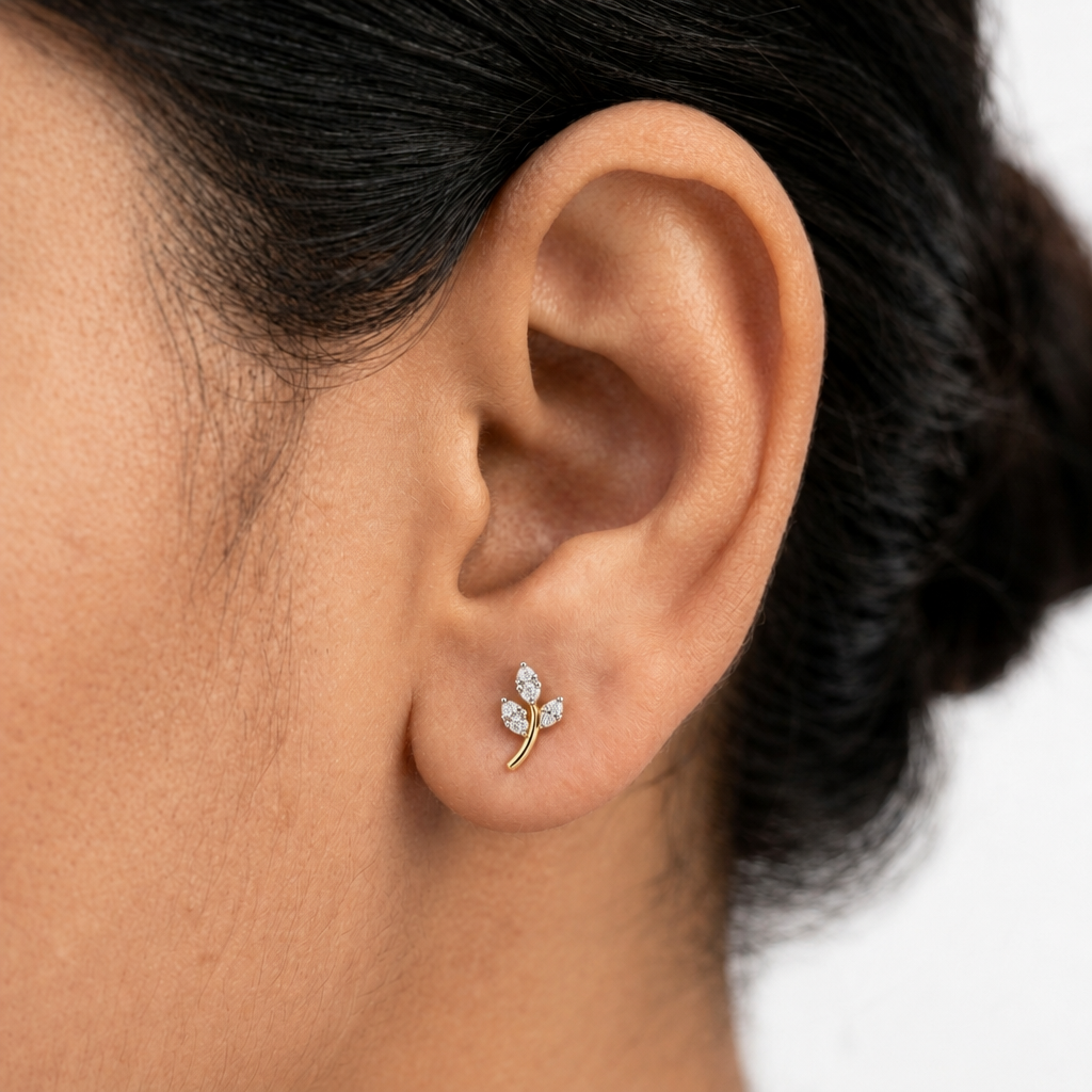  Close-up of a woman's ear wearing a 14k solid yellow gold leaf branch stud earring with natural diamond leaves, showing its dainty size.