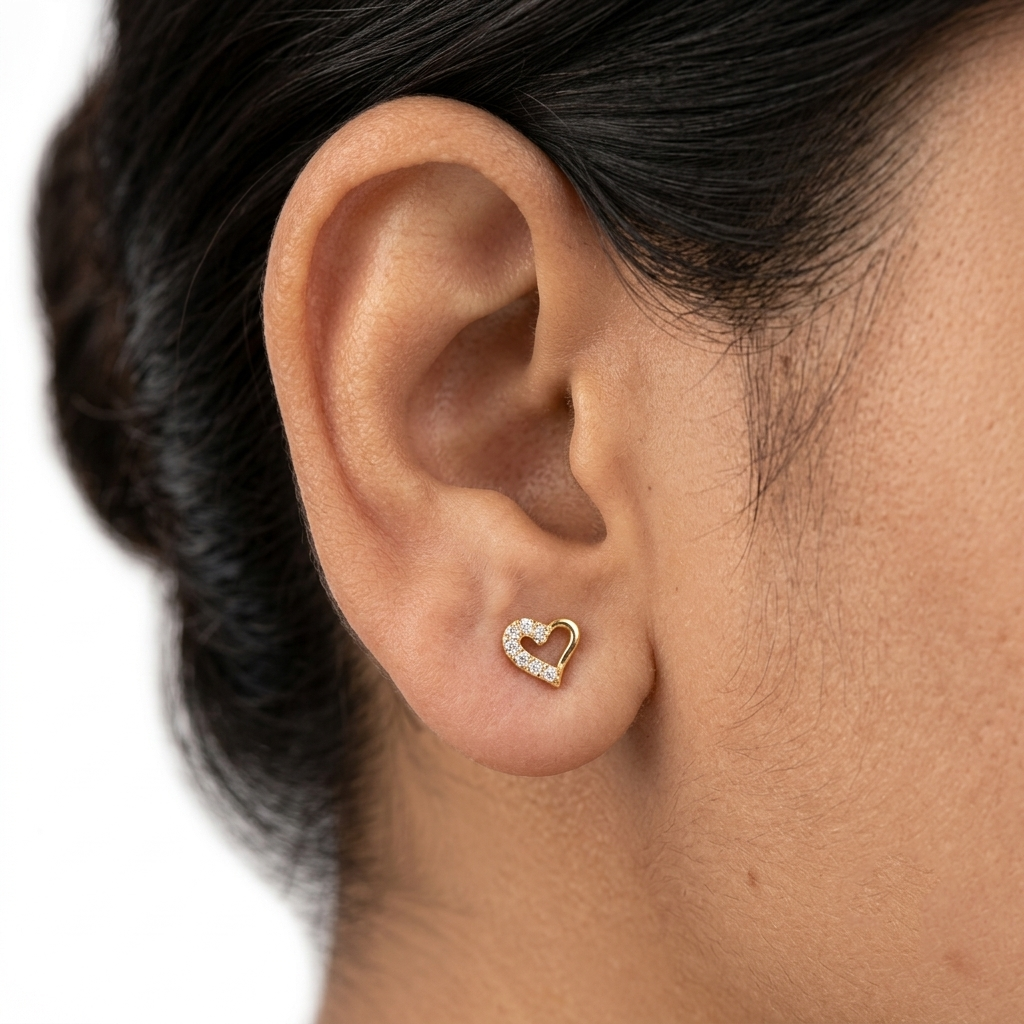 Close-up of a woman's ear wearing a 14k solid yellow gold open heart stud earring with pavé-set natural diamonds, showing its dainty size.