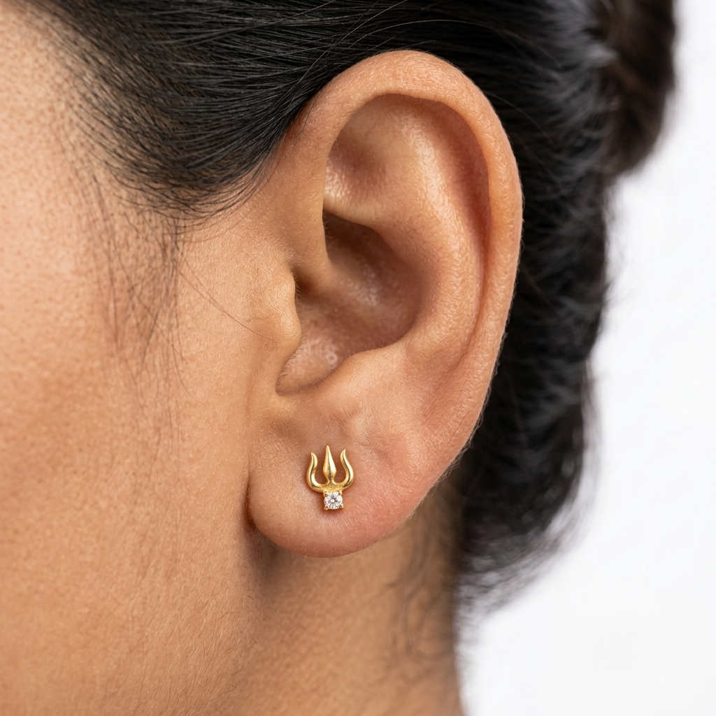 Close-up of a woman's ear wearing a 14k solid yellow gold trishul trident stud earring with a single natural diamond at the base, showing its dainty size.