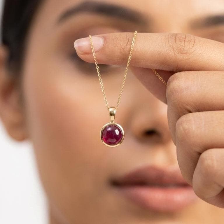 Close-Up of 14K Gold Natural Ruby Pendant Held by Model – Round Ruby Cabochon Bezel Necklace
