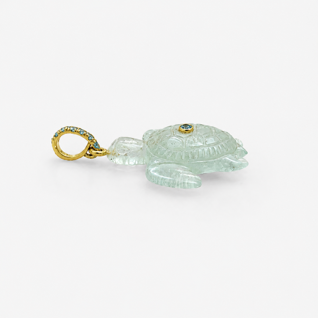 Hand-carved aquamarine sea turtle pendant in side profile facing left, with 14k yellow gold pavé ring bail set with Swiss blue topaz accents and bezel-set Swiss blue topaz on shell, translucent pale blue gemstone with engraved shell and flipper detail