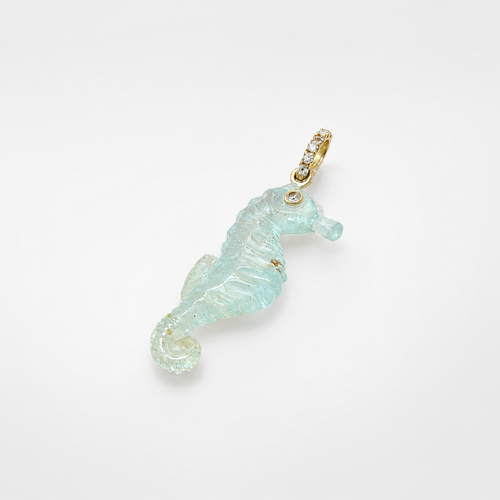 Hand-carved aquamarine seahorse pendant shown at diagonal angle facing right, with 14k yellow gold pavé ring bail set with white topaz accents and bezel-set white topaz eye, translucent pale seafoam blue gemstone with ribbed body and curled tail detail