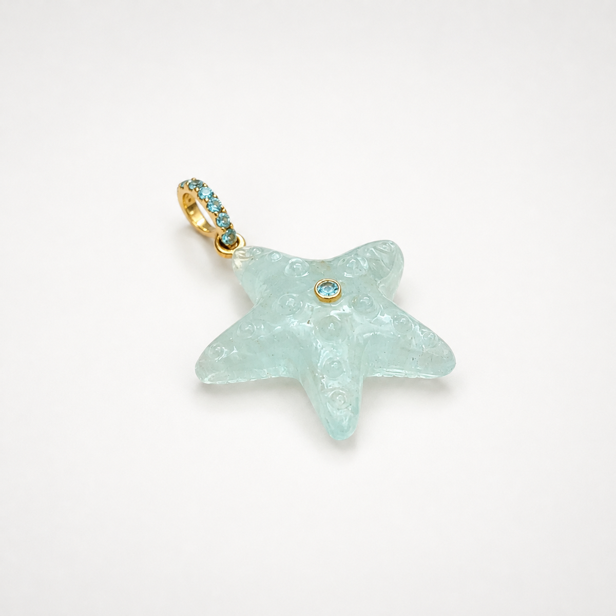 Hand-carved aquamarine starfish pendant at diagonal angle with bail at top left, 14k yellow gold pavé bail set with Swiss blue topaz accents and bezel-set Swiss blue topaz center accent, translucent pale seafoam blue gemstone with engraved bubble and swirl texture