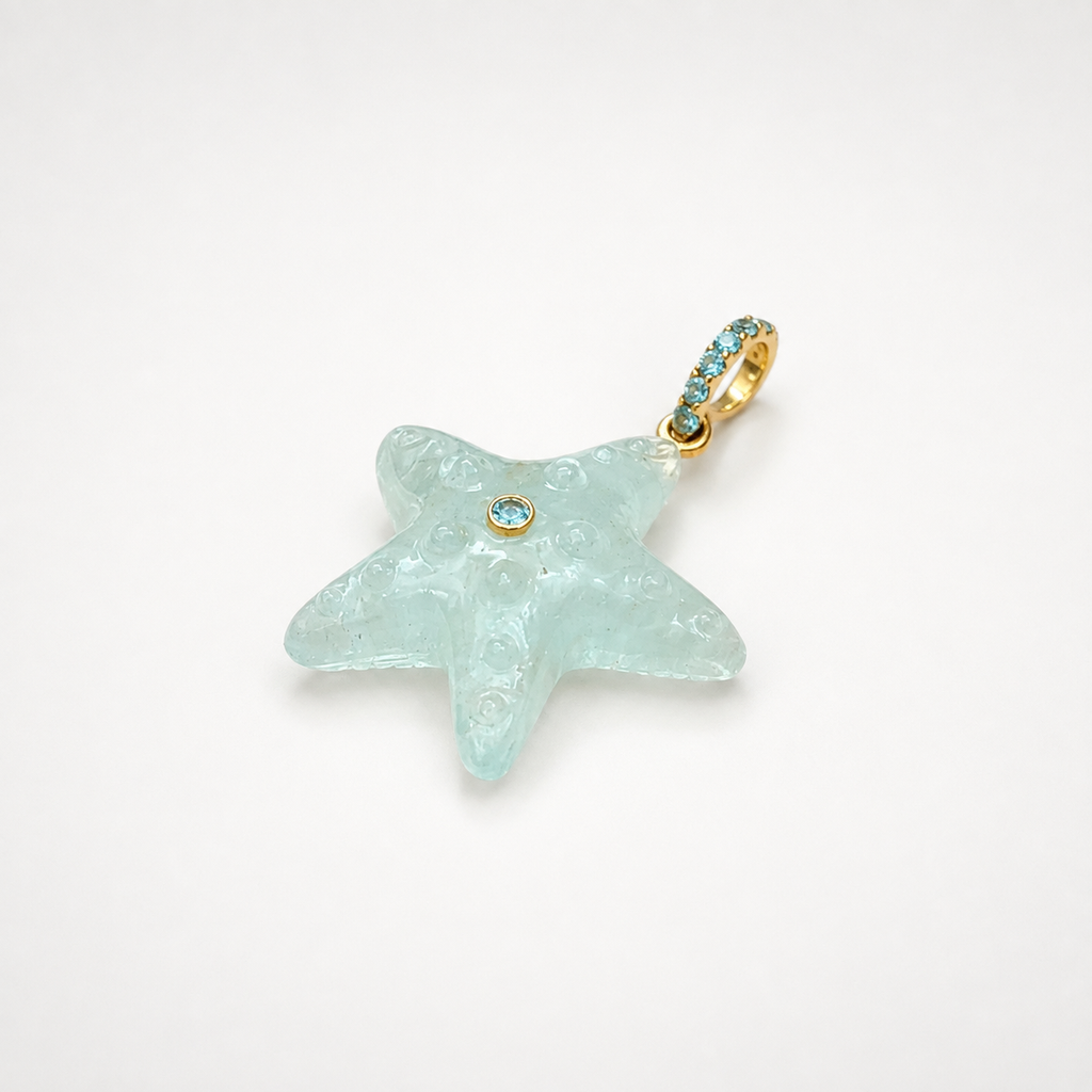 Hand-carved aquamarine starfish pendant at diagonal angle with bail at top right, 14k yellow gold pavé bail set with Swiss blue topaz accents and bezel-set Swiss blue topaz center accent, translucent pale seafoam blue gemstone with engraved bubble and swirl texture