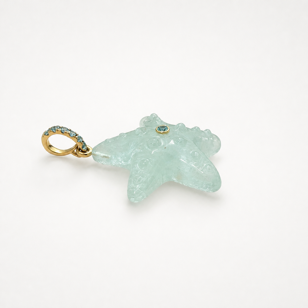 Hand-carved aquamarine starfish pendant in side profile showing back face and open ring bail at left, 14k yellow gold pavé ring bail set with Swiss blue topaz accents and bezel-set Swiss blue topaz center accent, translucent pale blue gemstone with raised bubble texture and natural inclusions
