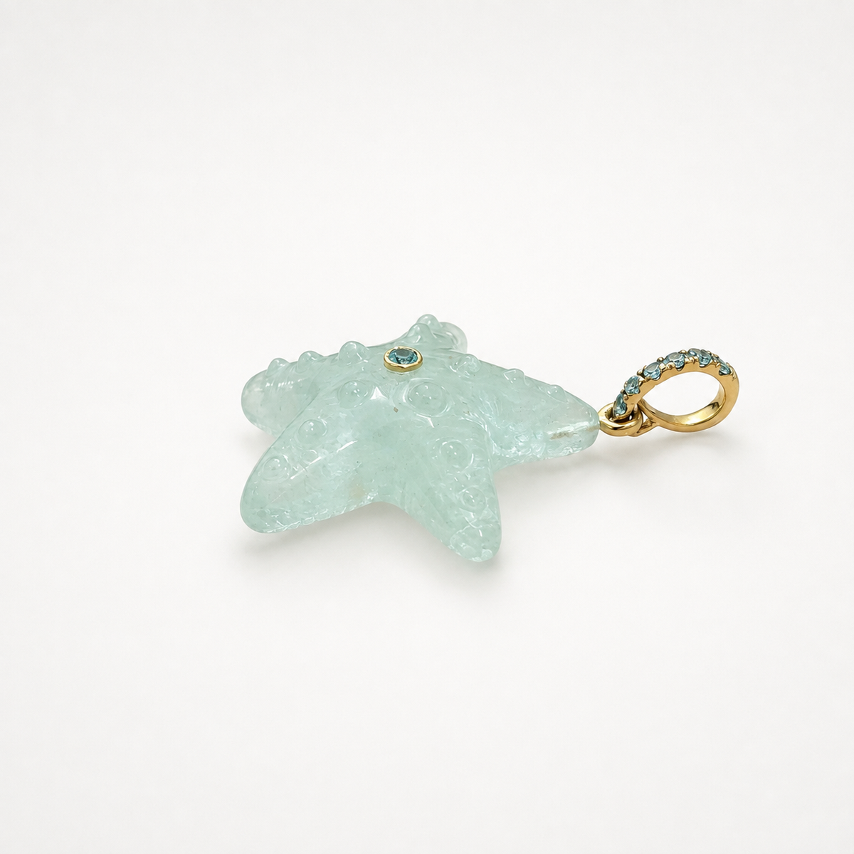 Hand-carved aquamarine starfish pendant in side profile showing back face and open ring bail at right, 14k yellow gold pavé ring bail set with Swiss blue topaz accents and bezel-set Swiss blue topaz center accent, translucent icy blue gemstone with raised bubble texture and natural inclusions

