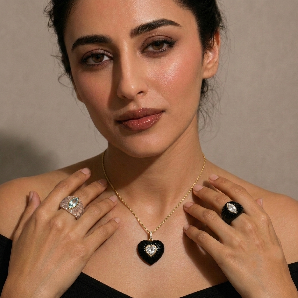 Editorial portrait of model with dark updo and slight smile wearing black onyx Aurelia heart pendant on 14k yellow gold chain with bezel-set heart-cut white topaz center stone, black onyx fluted ring with marquise white topaz on left hand and silver fluted ring with marquise white topaz on right hand, black off-shoulder top